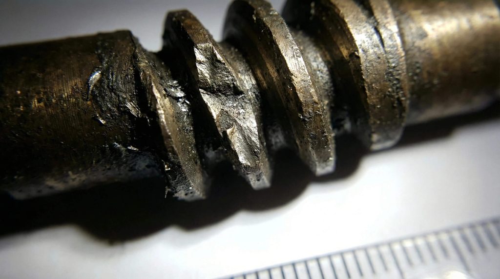 Macro shot showing severe wear, pitting, and metal fatigue on a damaged worm gear screw thread.